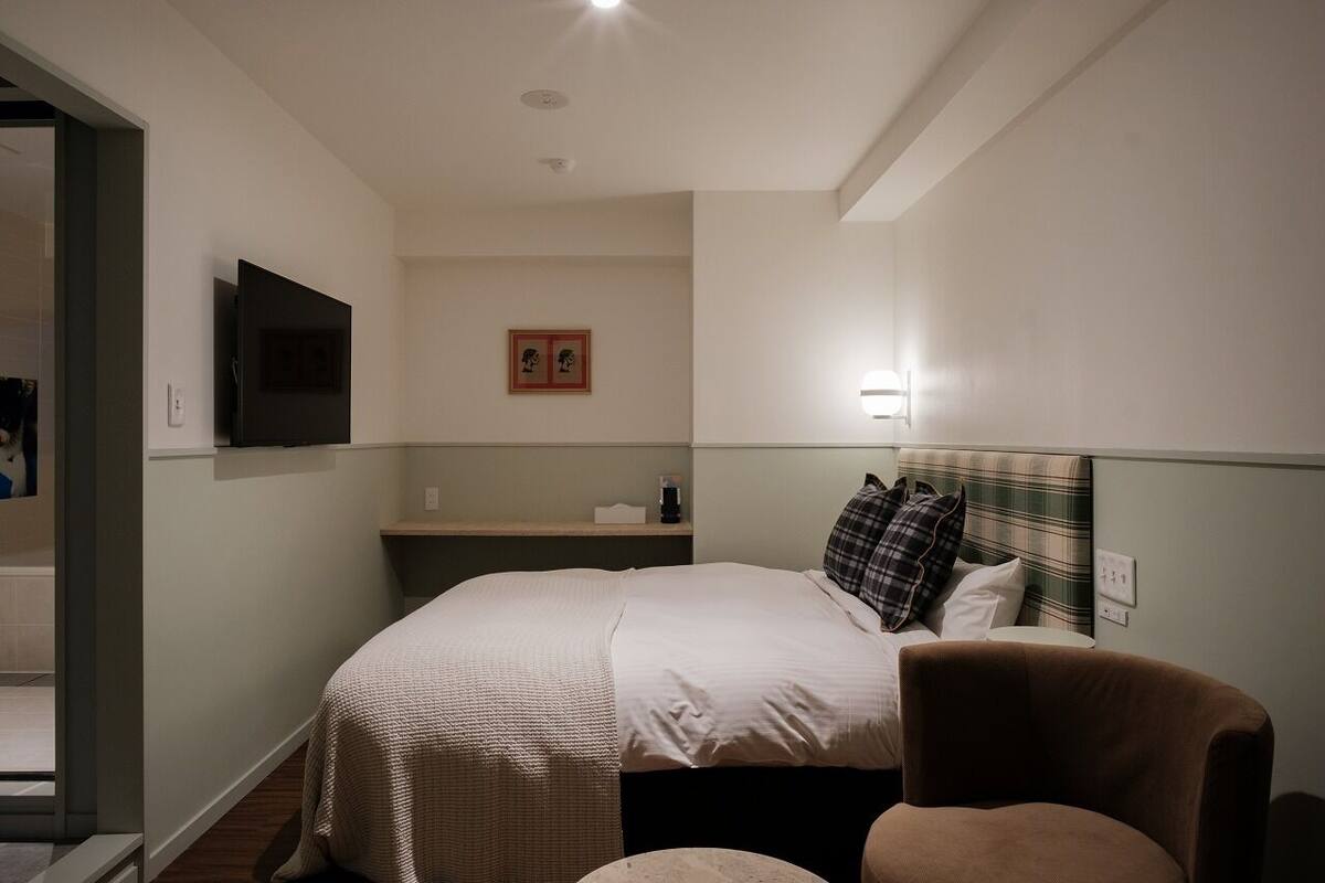 Een hotelkamer met een bed, een stoel, een televisie, een nachtkastje en een wandlamp.