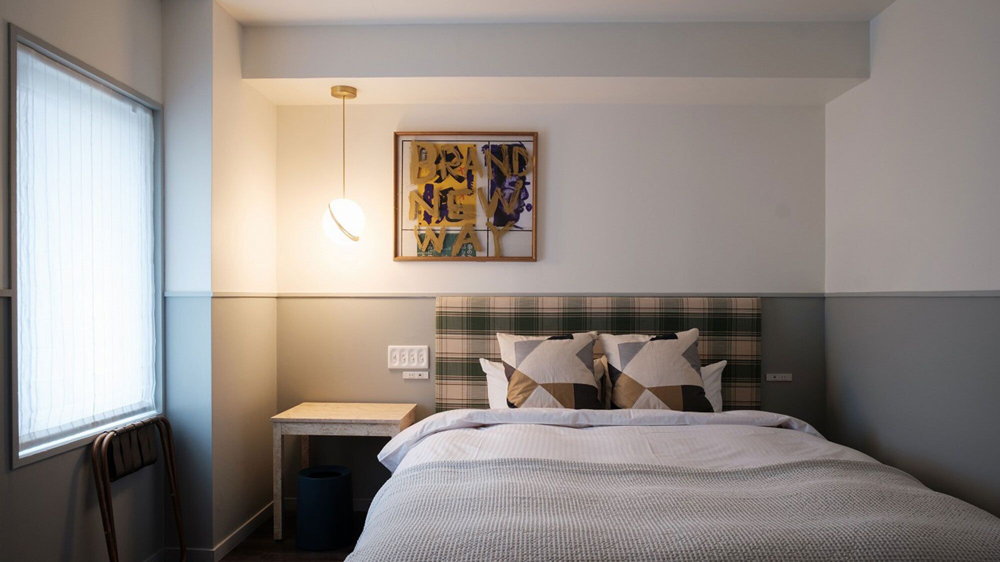 A hotel room with a bed, a bedside table, a wall-mounted light, and a framed artwork.