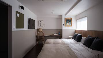 A hotel room with a bed, a desk, a chair, a picture on the wall, and a window.