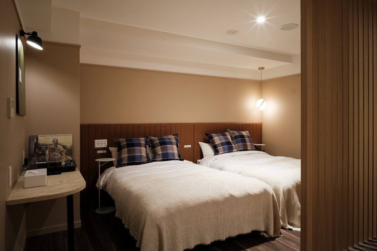 Een hotelkamer met twee bedden, een nachtkastje, een lamp en een poster aan de muur.