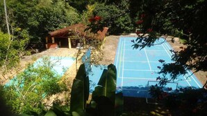 A view of a tennis court surrounded by lush greenery and a small building with a red roof. - An excellent place for rest and relaxation surrounded by nature. (Bragança Paulista)