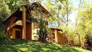 A two-story house with a brick exterior, a balcony, and a lush green garden. - An excellent place for rest and relaxation surrounded by nature. (Bragança Paulista)