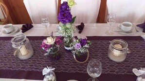 A table set with glass vases of flowers, a candle, and a small gift bag. - Wildkräuterhotel (Windelsbach)
