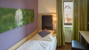 A single bed with a pillow and a headboard, a bedside table, a lamp, and a window with curtains.