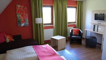 A hotel room with a bed, a desk, a chair, a TV, and a window with curtains.