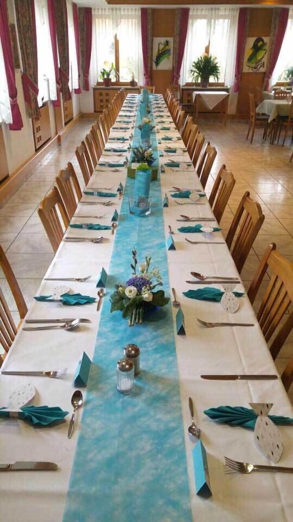 A long dining table set for a formal event with chairs on both sides, a blue floral runner, and centerpieces. - Wildkräuterhotel (Windelsbach)