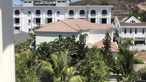 Un edificio blanco con techo de tejas, rodeado de vegetación y un paisaje montañoso.