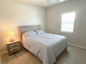 Une chambre à coucher avec un lit, une table de chevet avec une lampe et une fenêtre.