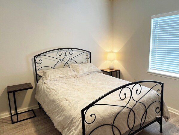 Een enkel bed met metalen frame en hoofdbord, een nachtkastje, een lamp en een raam met zonwering.