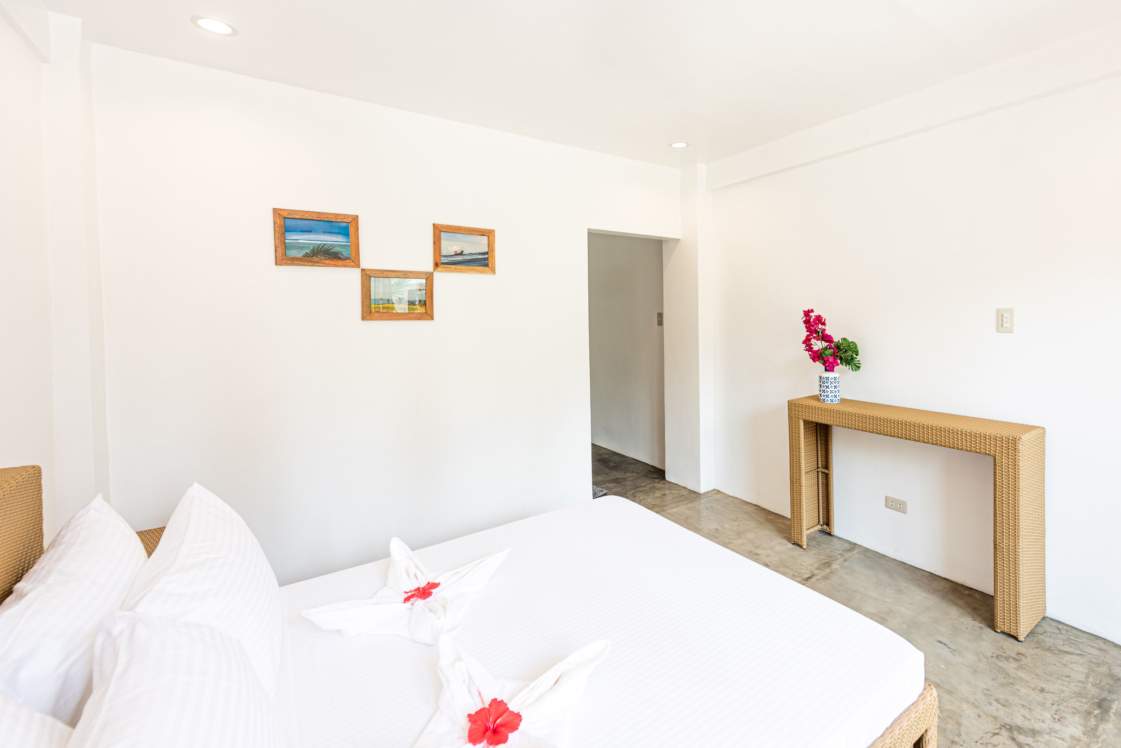 A hotel room with a bed, white walls, and a console table with a vase of flowers.