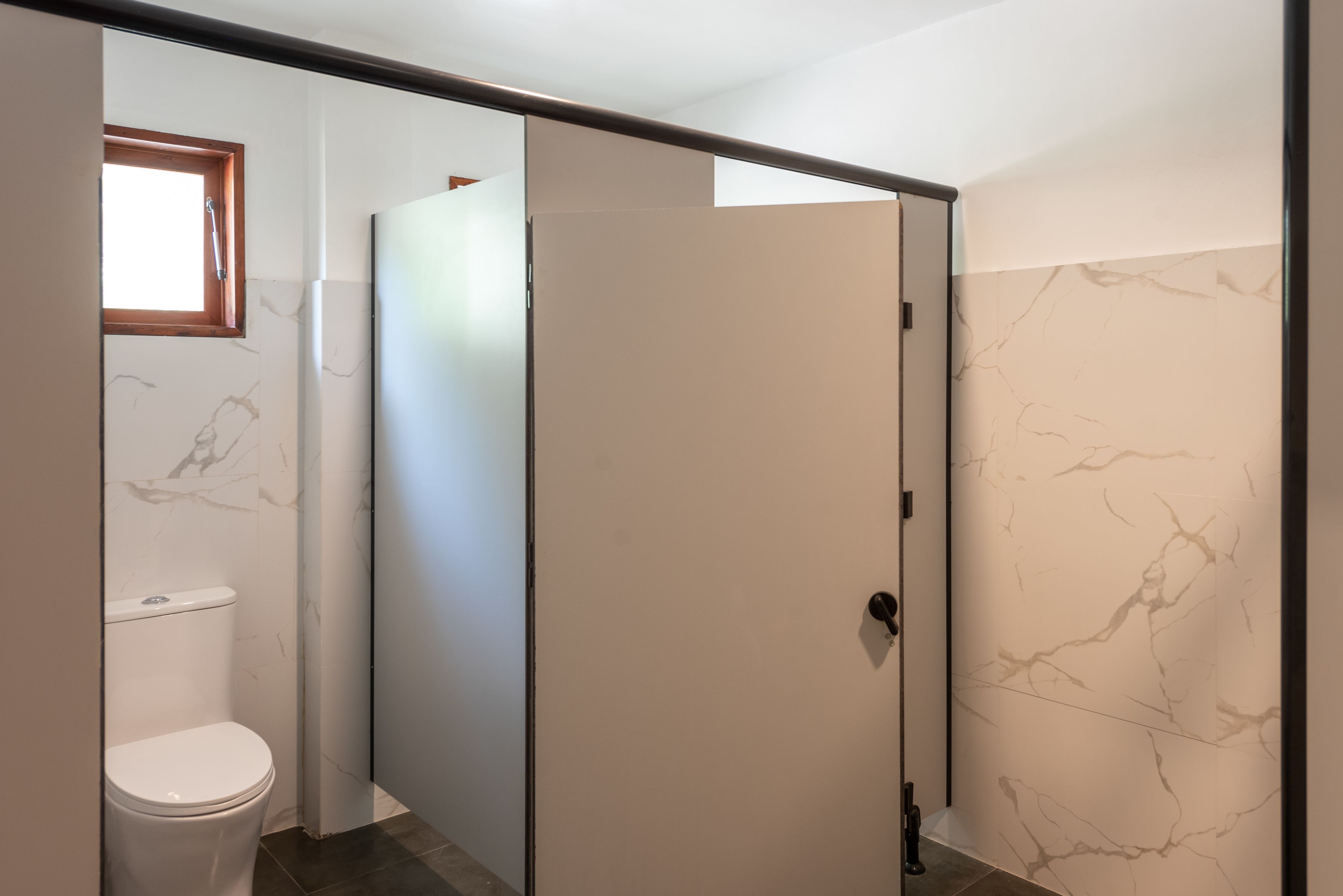 A bathroom with a toilet, a shower stall, and a door with a marble-patterned wall.