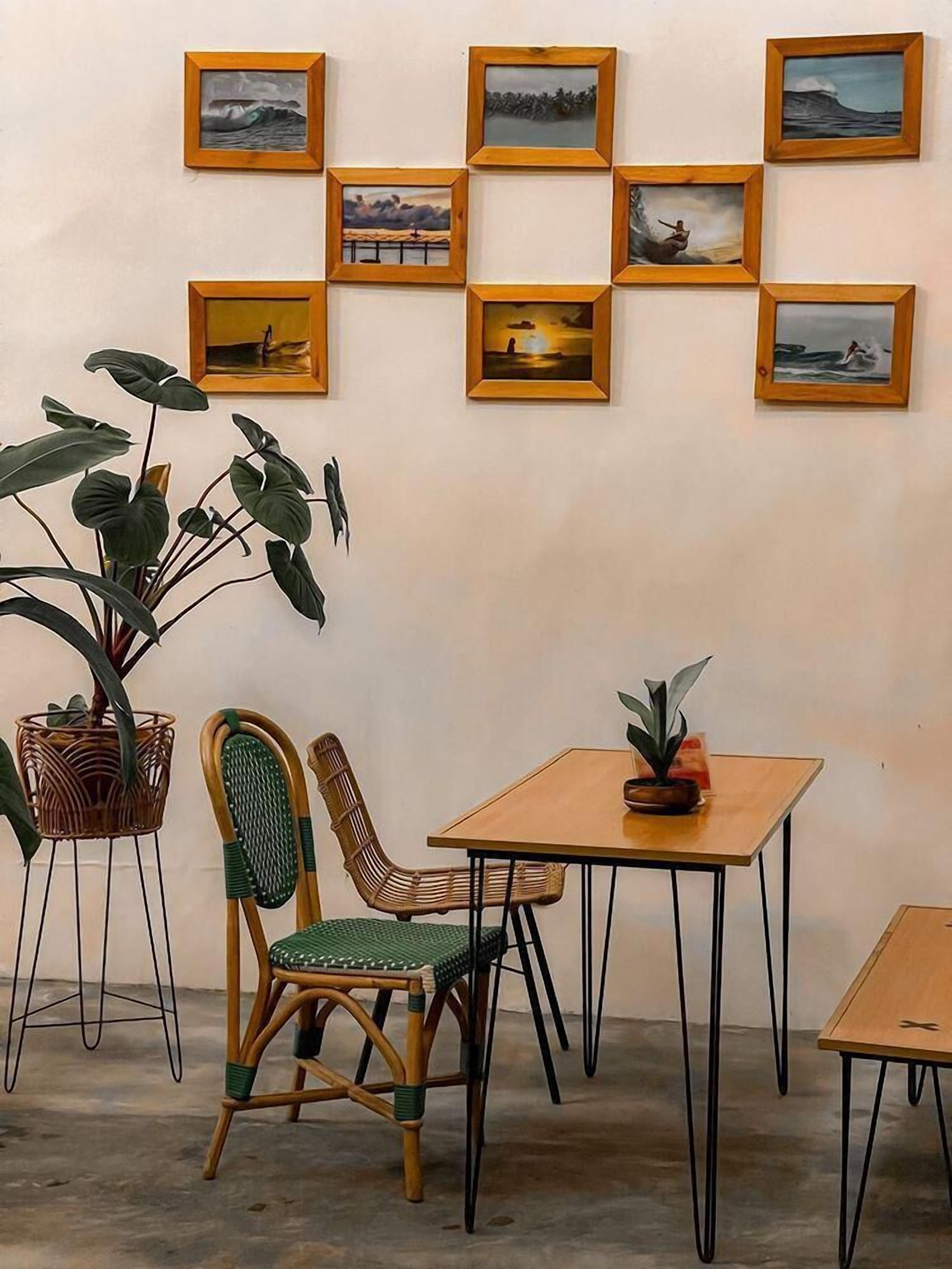 A dining area with a wooden table and two wicker chairs, a potted plant on the table, and a wall decorated with framed pictures.