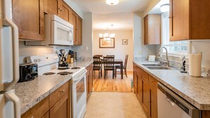 A kitchen with wooden cabinets, a microwave, a stove, and a dishwasher. There is a dining table with chairs and a chandelier above it. - Minutes to Airport, Waterfront and Downtown Sleeps 6 (Bellingham)