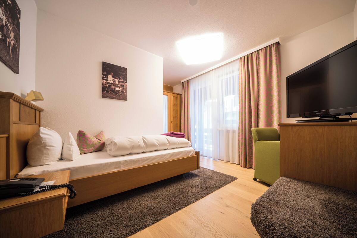 Una habitació moderna amb un llit, una televisió, una taula i una cadira.