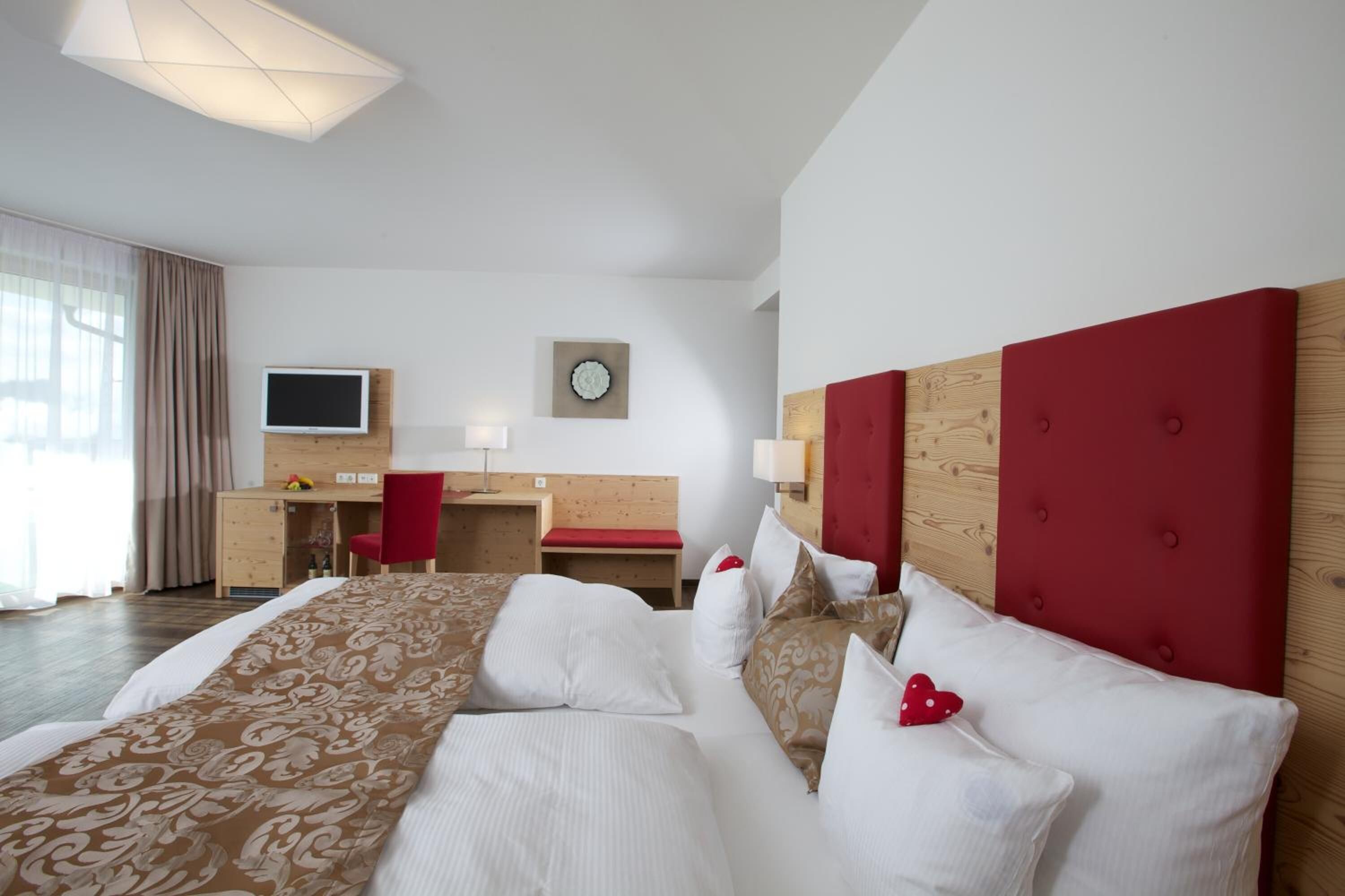 A hotel room with a large bed, a desk, a TV, and a window with curtains.