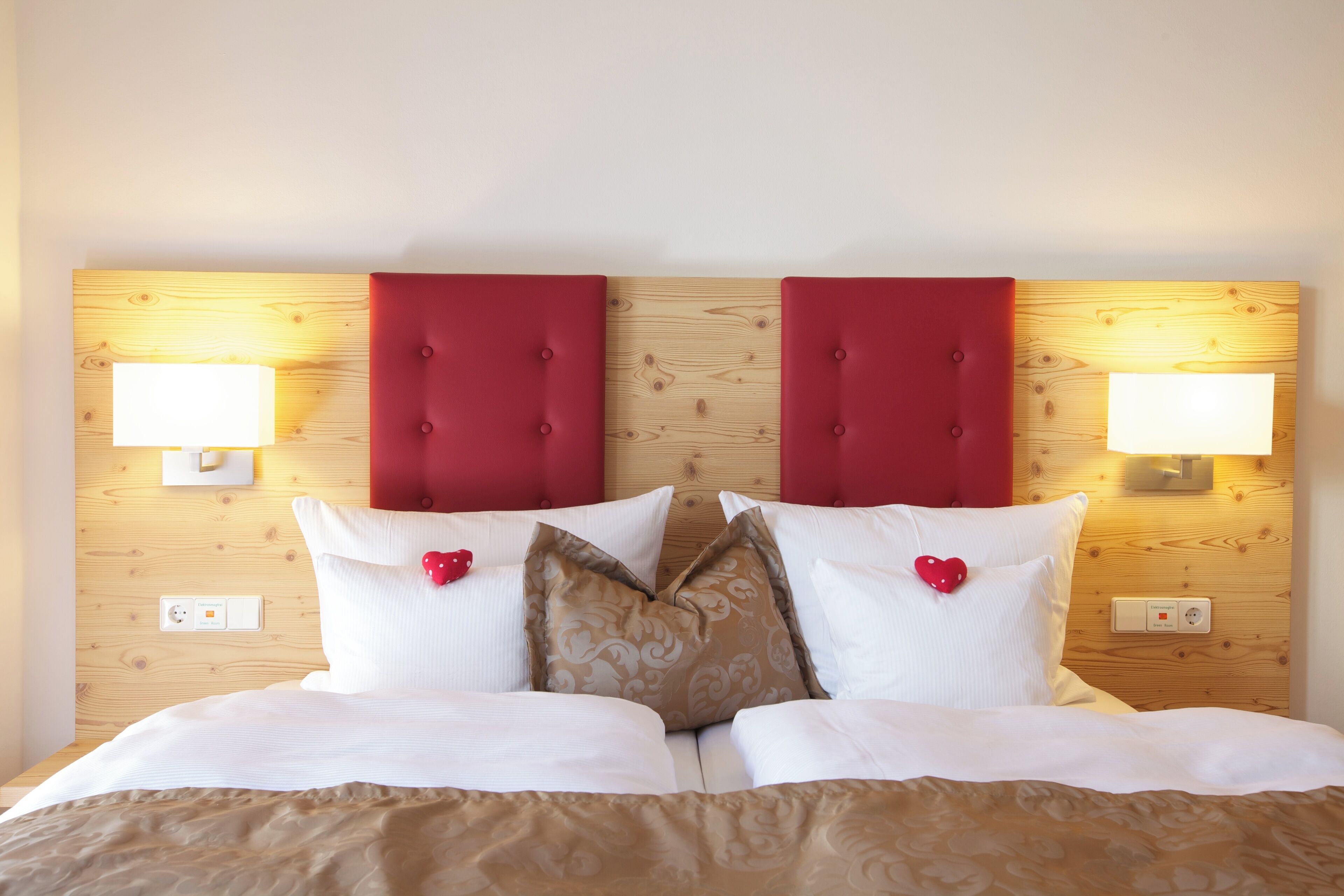 A double bed with a wooden headboard, two bedside lamps, and heart-shaped pillows.