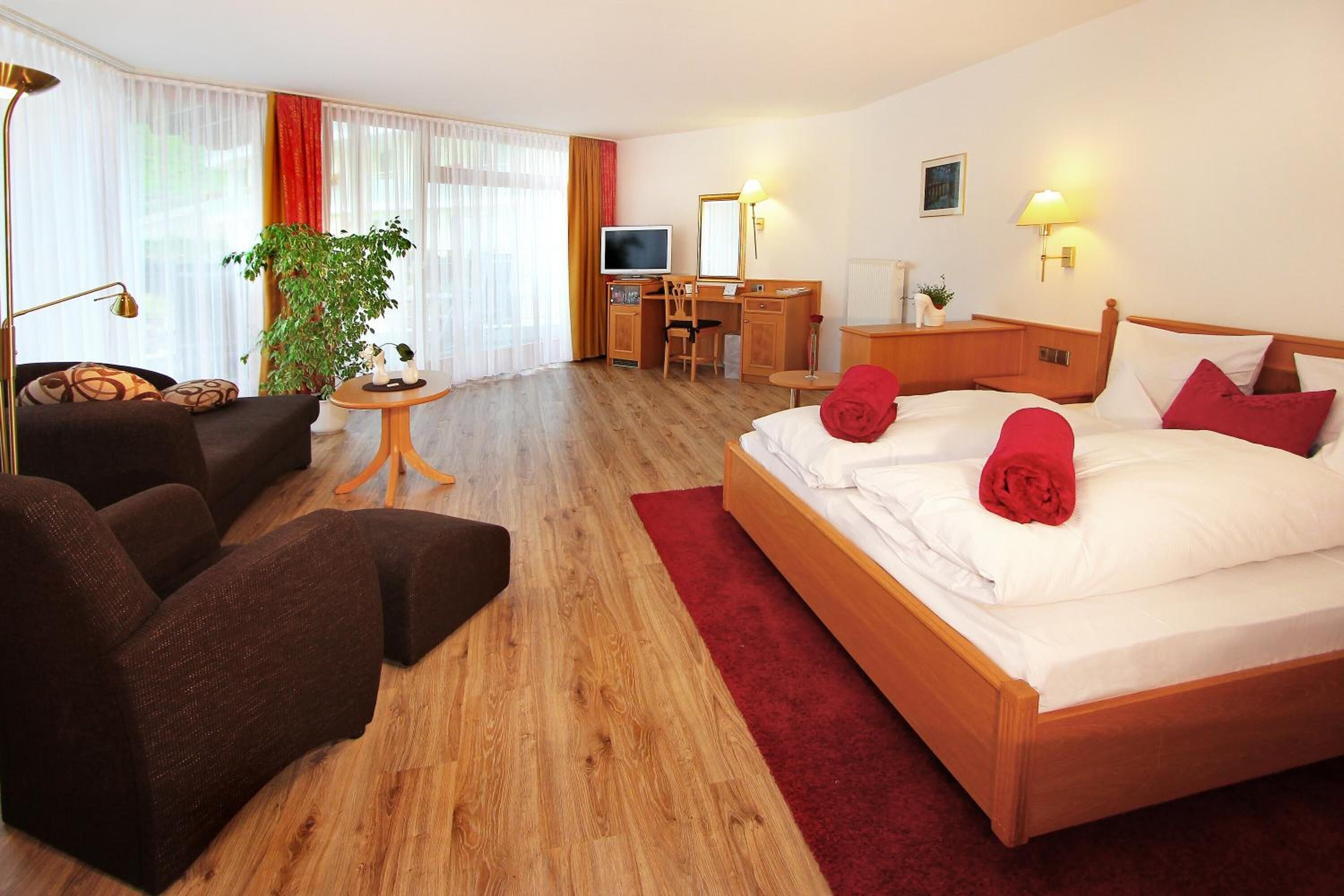 Une chambre d’hôtel avec un lit, un bureau, une chaise, une télévision et une plante.