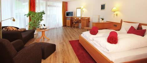 Une chambre d’hôtel avec un lit, un bureau, une chaise, une télévision et une plante.