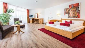 A hotel room with a wooden bed, a desk, a chair, a sofa, and a large window with curtains.
