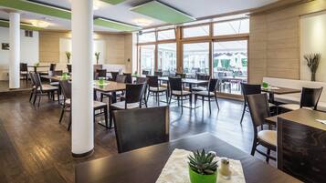 Un restaurante moderno con suelo de madera, paneles de techo verdes y grandes ventanales que ofrecen vistas al exterior.