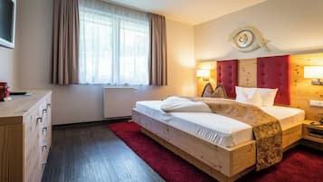 Habitación de hotel con cama de madera, alfombra roja, cómoda de madera, ventana con cortinas y un adorno en la pared con forma de ojo.