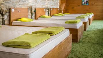 A row of neatly made beds with green towels, wooden headboards, and a brick wall in the background.