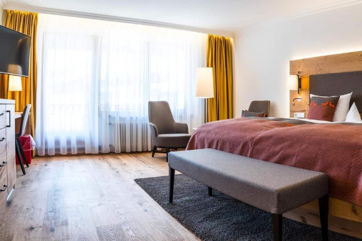 Habitació d'hotel moderna amb un llit gran, una banca, escriptori i televisió.