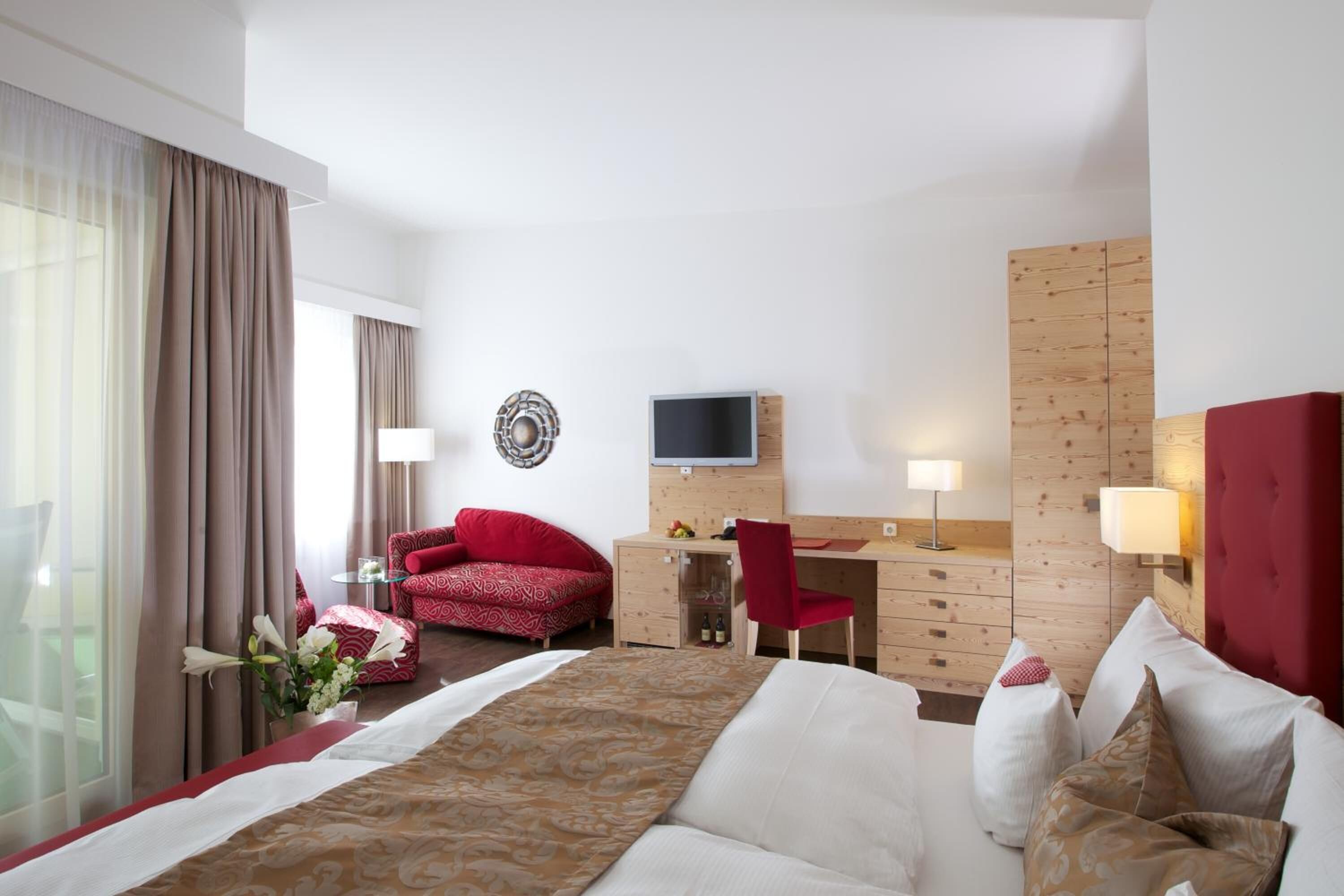 Een hotelkamer met een bed, een bureau, een rode fauteuil, een televisie en een houten garderobe.