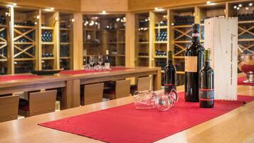 A wine tasting room with wooden shelves, a long table with a red placemat, wine bottles, and glasses.