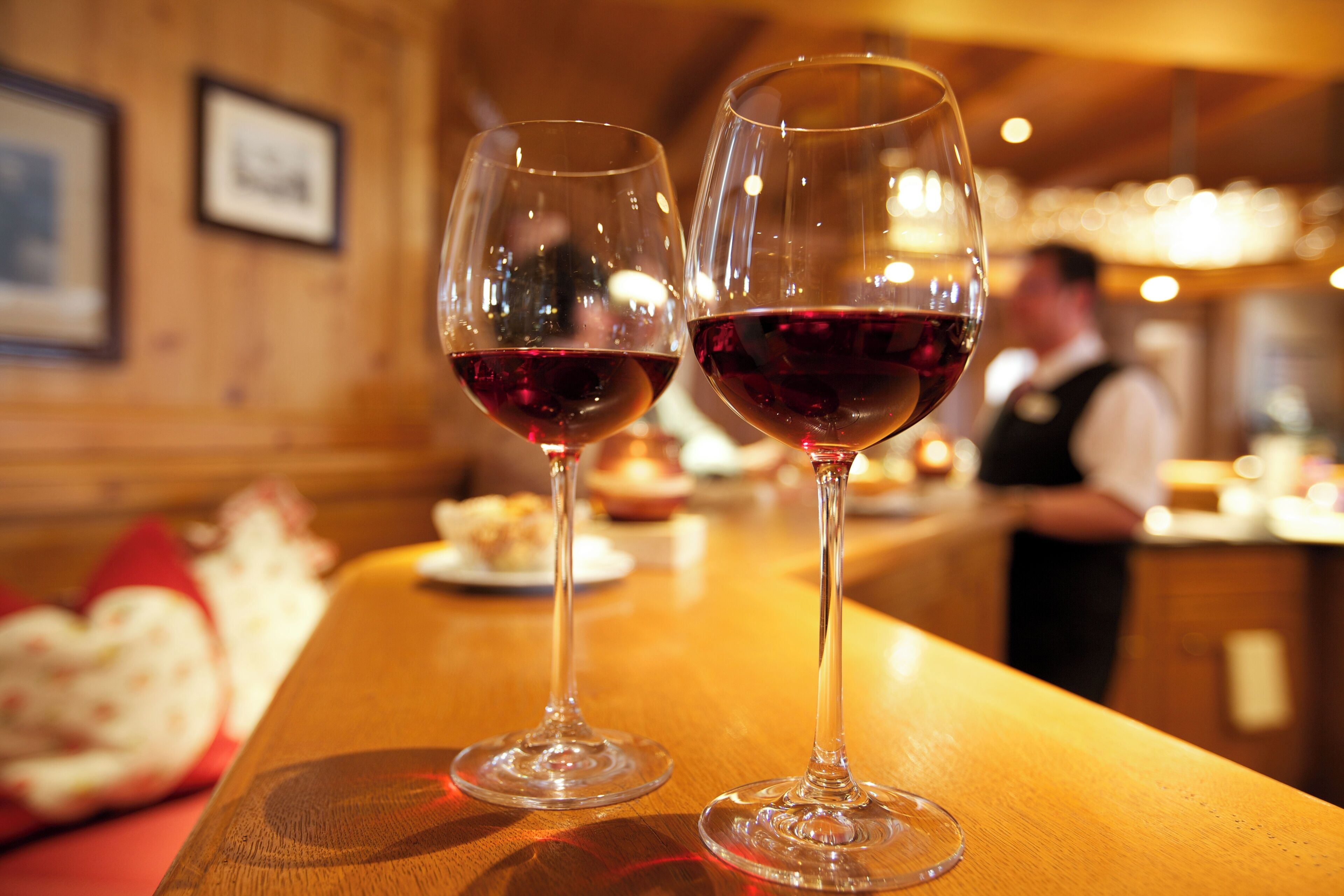 Deux verres à vin sur le comptoir en bois d’un bar, avec un arrière-plan flou représentant l’ambiance d’un restaurant.