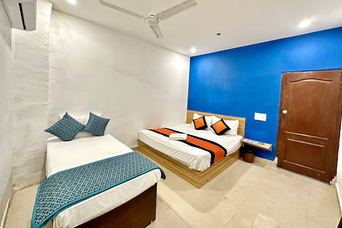 Un dormitorio con dos camas, un ventilador de techo, una puerta de madera y una pared azul decorativa.