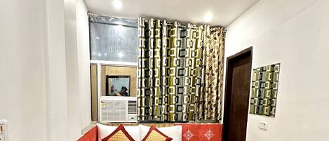 Una camera da letto con un letto, una ventola a soffitto, tende a motivi decorativi e una finestra con condizionatore.