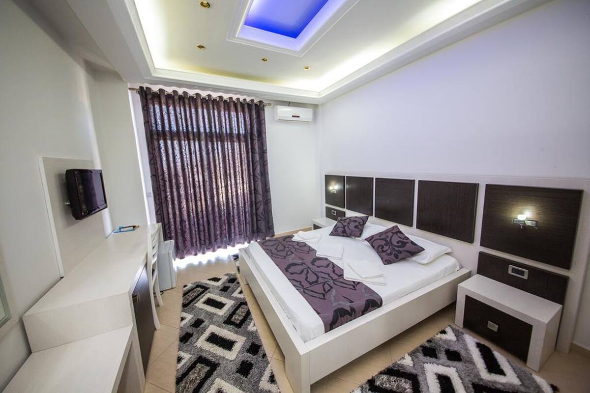Un dormitorio moderno con un tragaluz, una cama con ropa de cama estampada, una mesita de noche y un televisor montado en la pared.