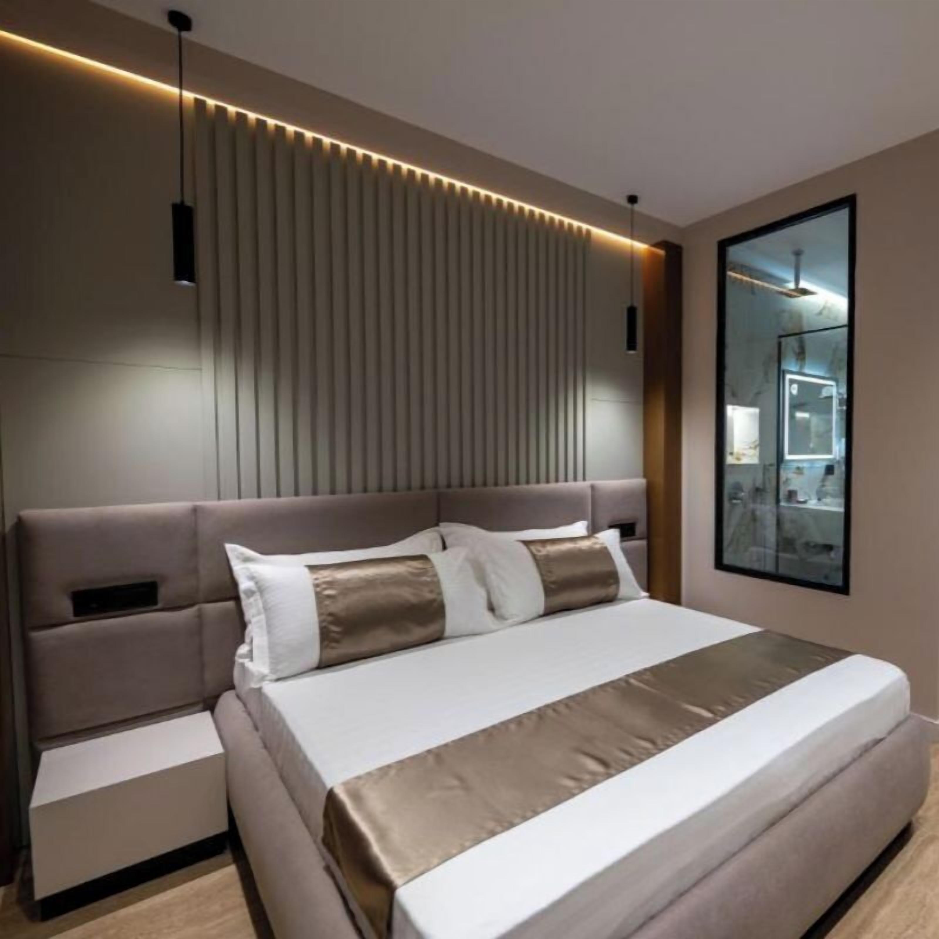 A modern bedroom with a large bed, bedside tables, a headboard with vertical slats, and a mirror on the wall.