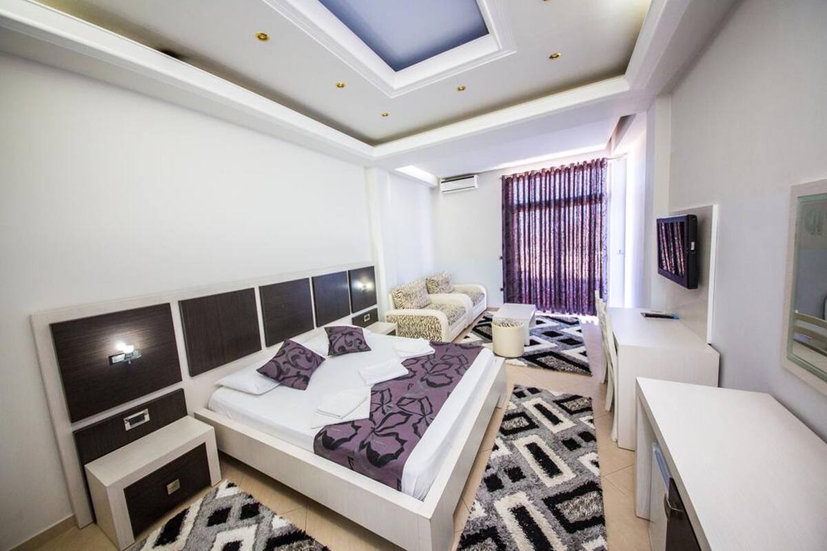 Un dormitorio moderno con tragaluz, una cama con ropa de cama estampada, un sofá, un televisor y un escritorio.