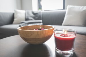 En träskål med blommor står på ett bord bredvid ett tänt ljus.