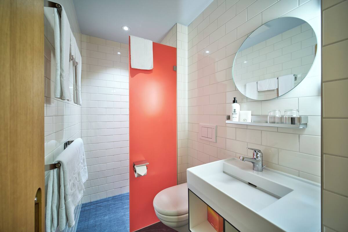 A modern bathroom with white and red tiles, a round mirror, a white sink, and a toilet.