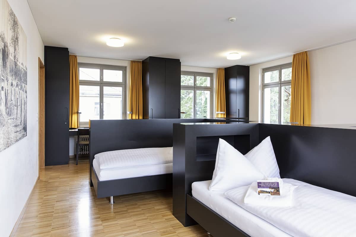 A modern hotel room with two beds, a desk, and large windows with curtains.