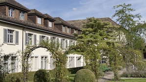 A row of traditional European-style buildings with white facades and dark roofs, surrounded by well-maintained gardens and a clear sky. - Hotel Arenenberg (Salenstein)