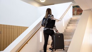 A person descending a staircase with a suitcase, wooden panel walls, and a painting on the wall. - Hotel Arenenberg (Salenstein)