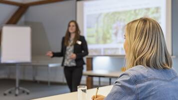 A conference room with a presentation screen, a whiteboard, and a table with a glass of water and a notepad.
