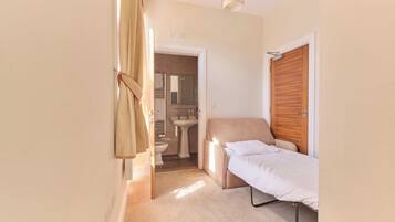 A compact room with a single bed, a small bedside table, a wooden wardrobe, a bathroom with a sink and toilet, and a shower area.