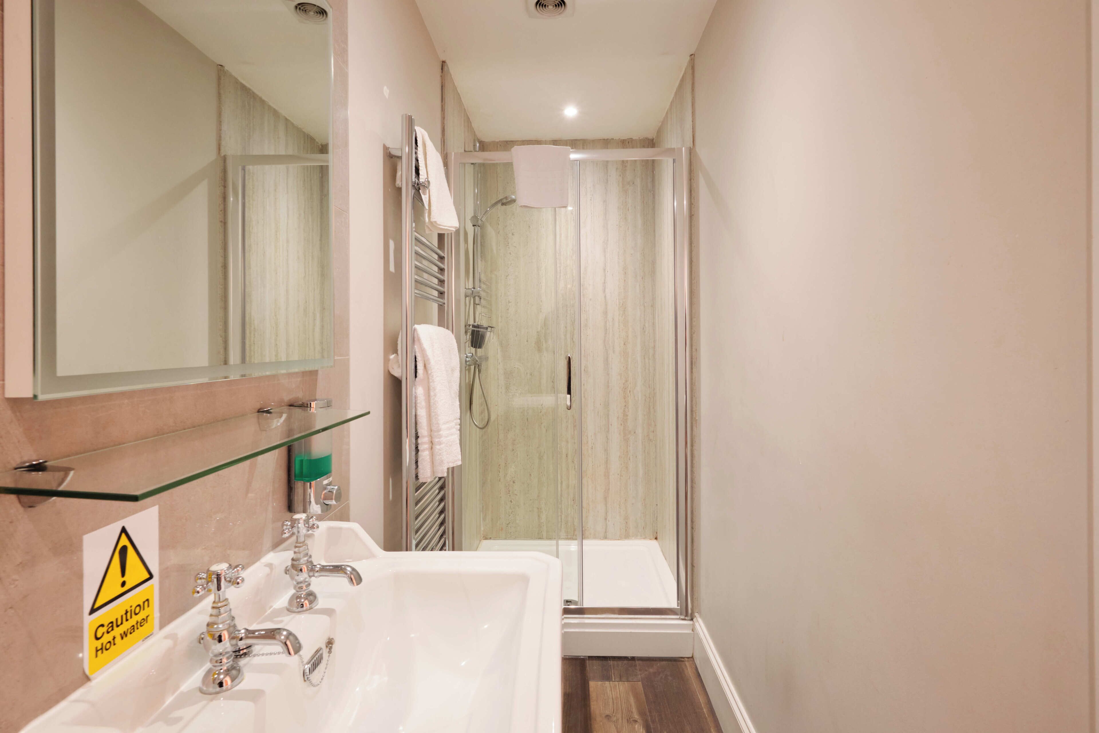 A bathroom with a sink, mirror, and a glass shower enclosure.