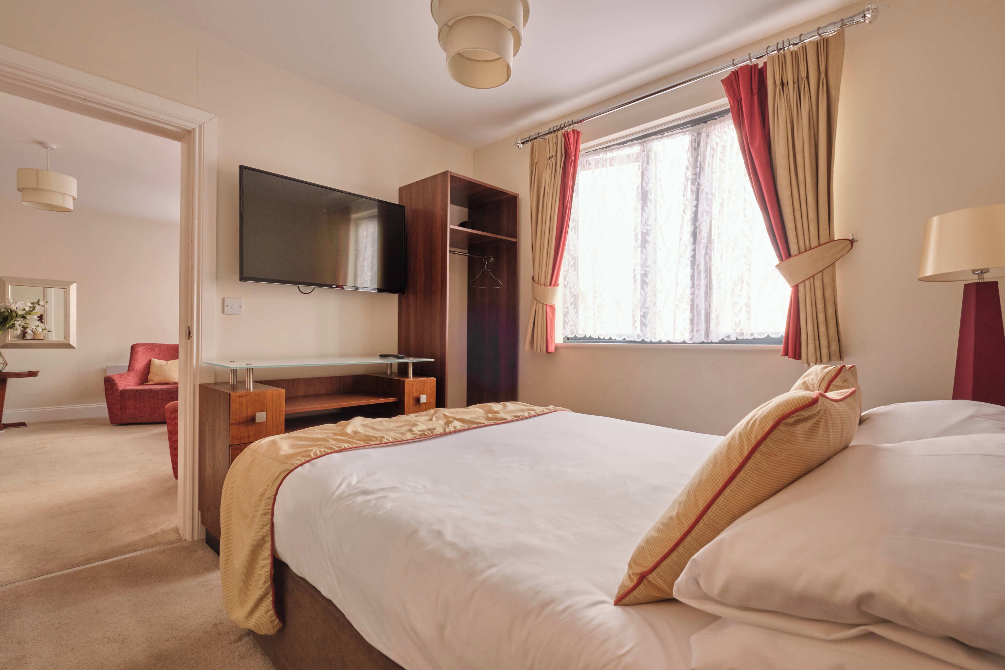 A hotel room with a bed, a TV mounted on the wall, a desk, and a wardrobe.