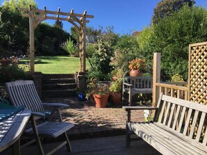 A wooden pergola, outdoor seating, and potted plants in a garden setting. - Anne's House (Hastings)