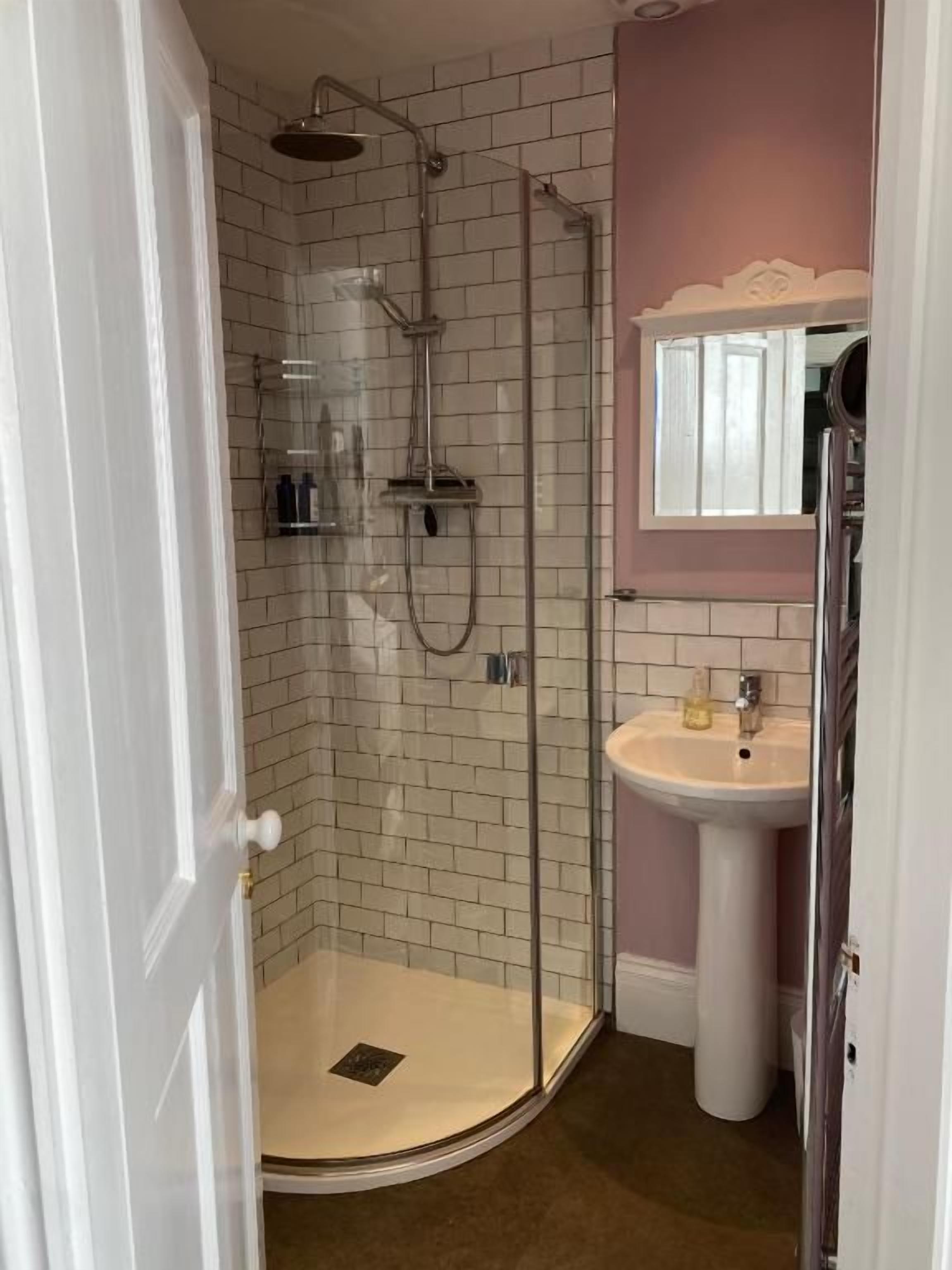 Un baño con ducha de vidrio, lavamanos pedestal y espejo sobre él.