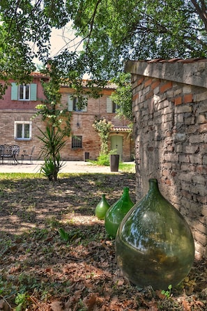 A courtyard with a brick wall, a green glass bottle, and a building with a tiled roof in the background.