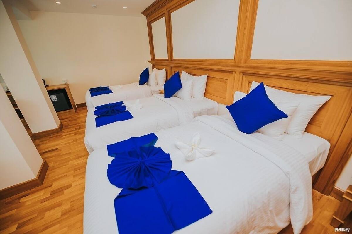 A hotel room with four beds, each with white bedding and blue accents, wooden headboard, and a wooden floor.