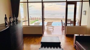 Una habitación con un ventanal grande que da a una piscina y al océano. Hay un sofá de cuero, una mesita con copas de vino y un banco de madera.