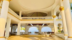 Un amplio vestíbulo de hotel con columnas blancas y un balcón con vista a la playa.